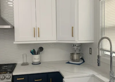 A modern kitchen featuring handleless cabinets, a white countertop, and stainless steel appliances.
