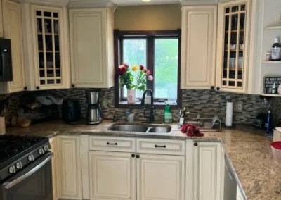 A bright kitchen with large windows, white cabinets, and a subway tile backsplash.